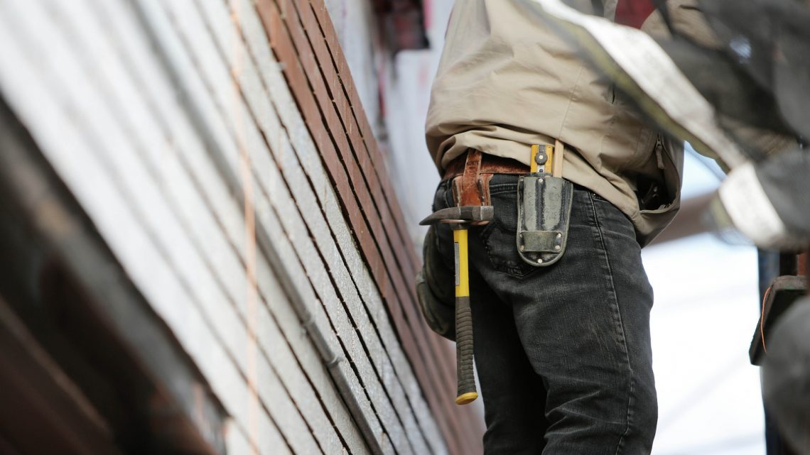 Partial view of person wearing jeans, workshirt, and toolbelt with hammer hanging from it