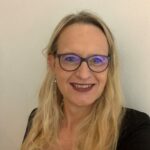 Headshot of a smiling white woman with long blond hair and glasses